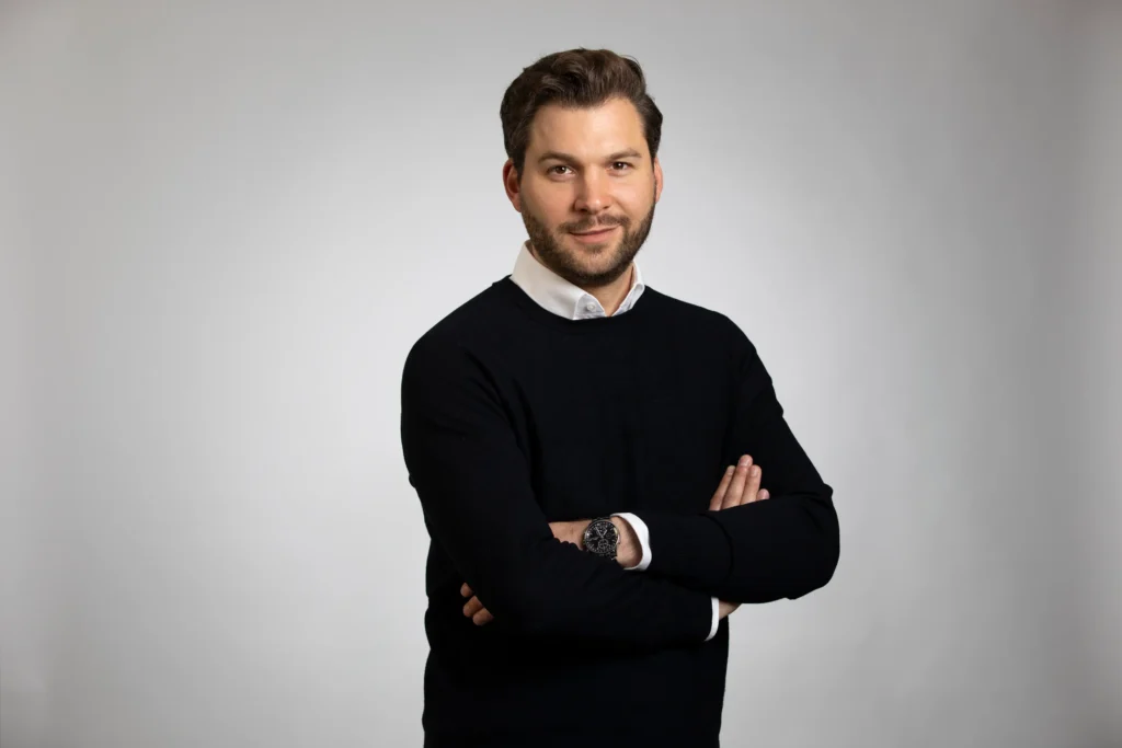 Die Grafik zeigt ein seriöses Profilbild des Finanzberaters Jens-Frederik Becker mit verschränkten Armen, der für ZSH Zahnärzte betreut.
