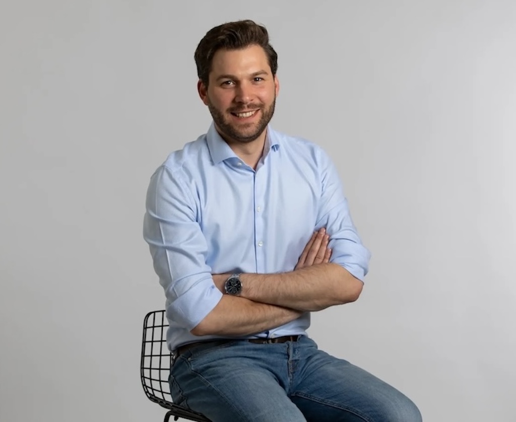 Die Grafik zeigt den Finanzberater Jens-Frederik Becker lächelnd auf einem Stuhl sitzen