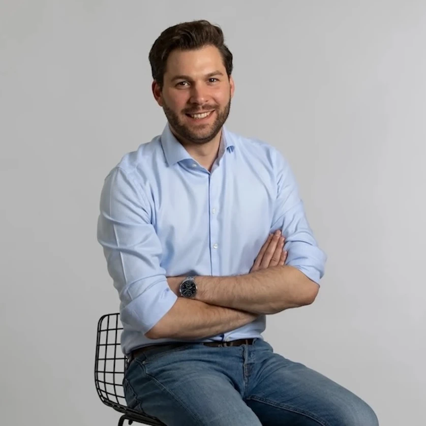 Die Grafik zeigt den Finanzberater Jens-Frederik Becker lächelnd auf einem Stuhl sitzen